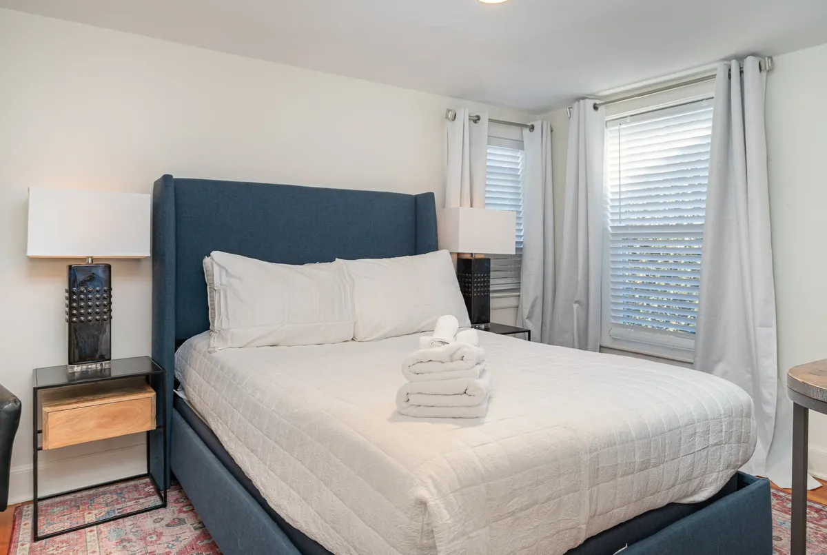 A serene bedroom with a plush queen bed, soft linens, and coordinated nightstands with lamps. The room features elegant curtains and a tranquil ambiance, ideal for restful evenings and peaceful mornings.