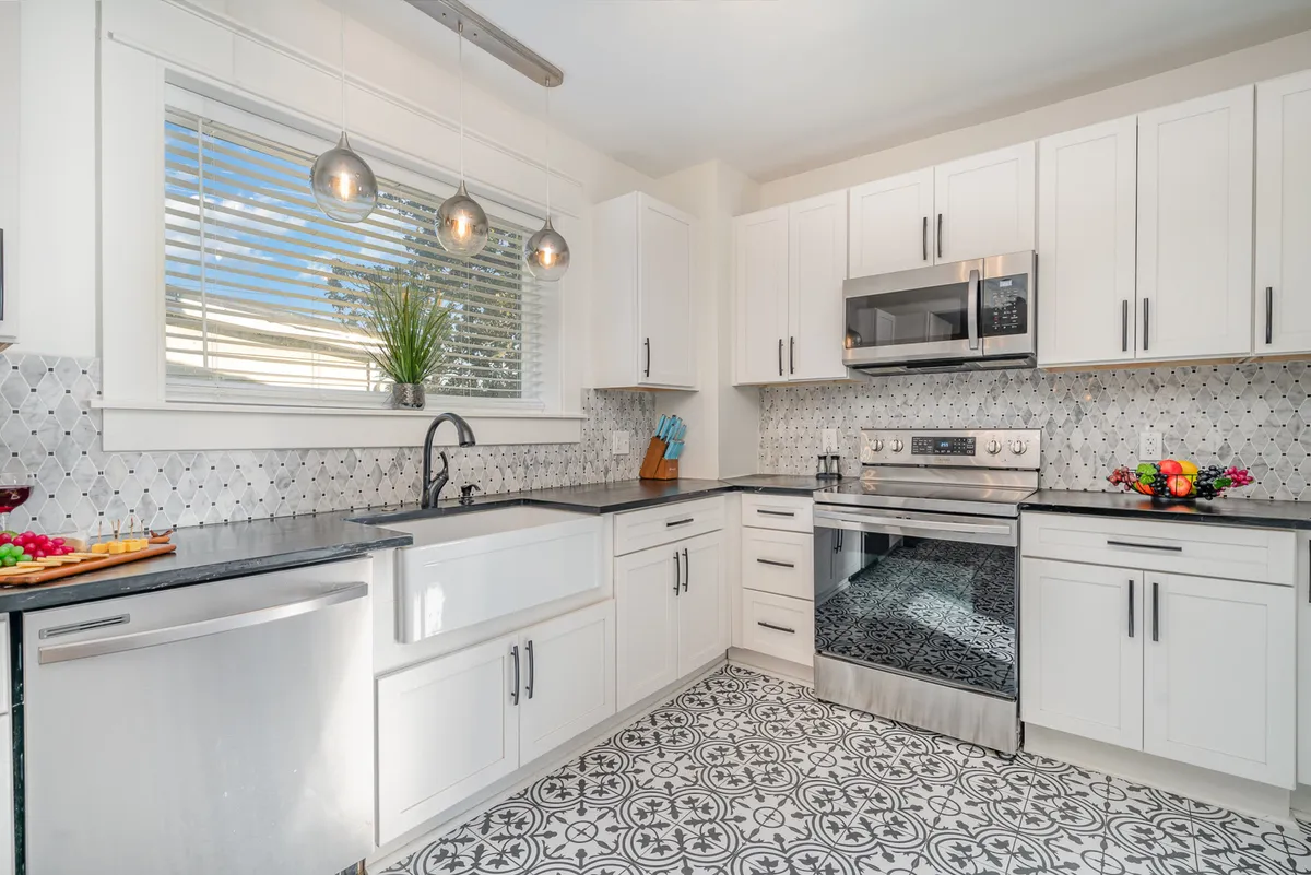 This kitchen scene highlights stainless steel appliances, a black countertop, decorative tile flooring, and a central island. The space is inviting and functional, perfect for preparing meals and gathering around for conversation.