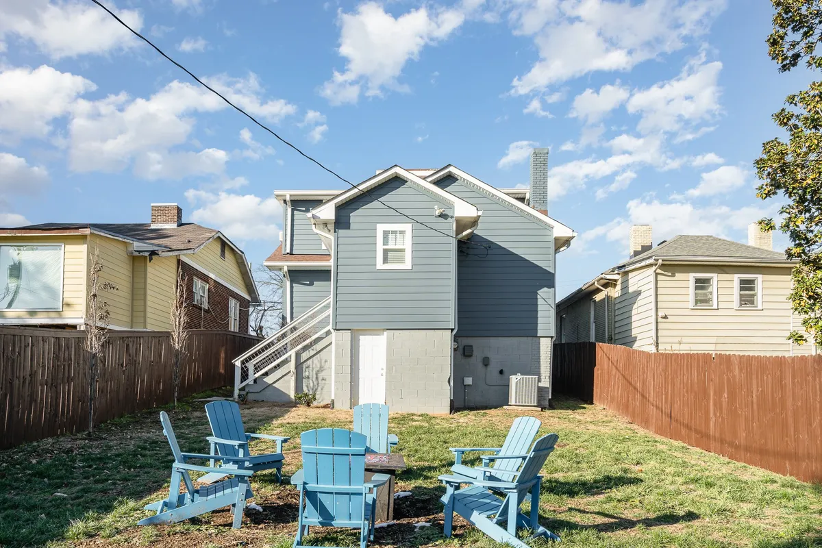This exterior shot showcases the yard’s blue Adirondack chairs encircling a fire pit, with the house visible in the background. The scene evokes warmth, togetherness, and the simple pleasure of spending time outdoors, day or night.