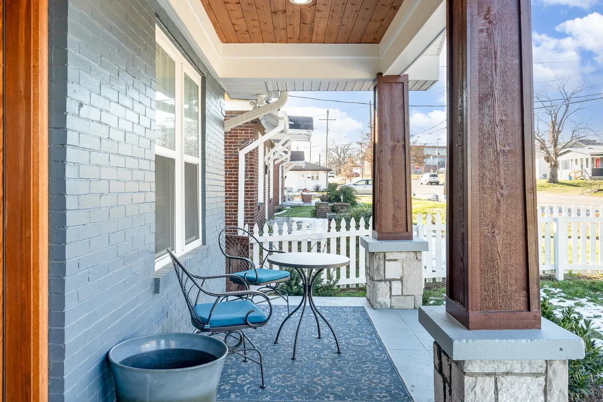 An inviting front porch with a swing, table and chairs, decorative stone columns, and a potted plant. The space is ideal for savoring morning coffee or enjoying quiet moments outdoors, with its welcoming and homey feel.